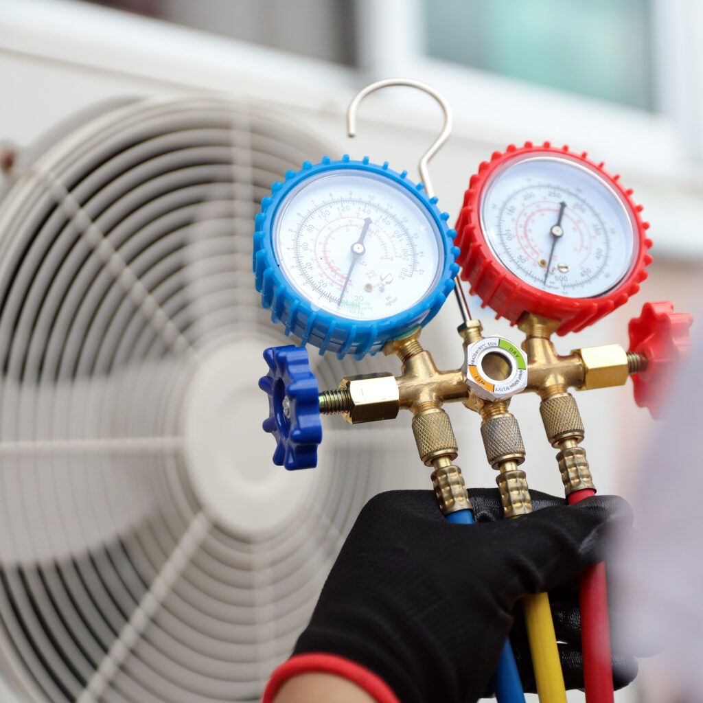 HVAC technician using manifold gauges to check an air conditioning unit.